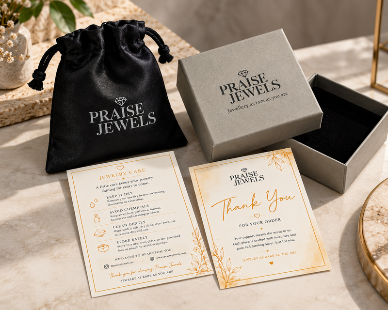 Jewelry care and thank-you cards from Praise Jewels displayed next to a black drawstring pouch and an open gray presentation box on a light marble surface.