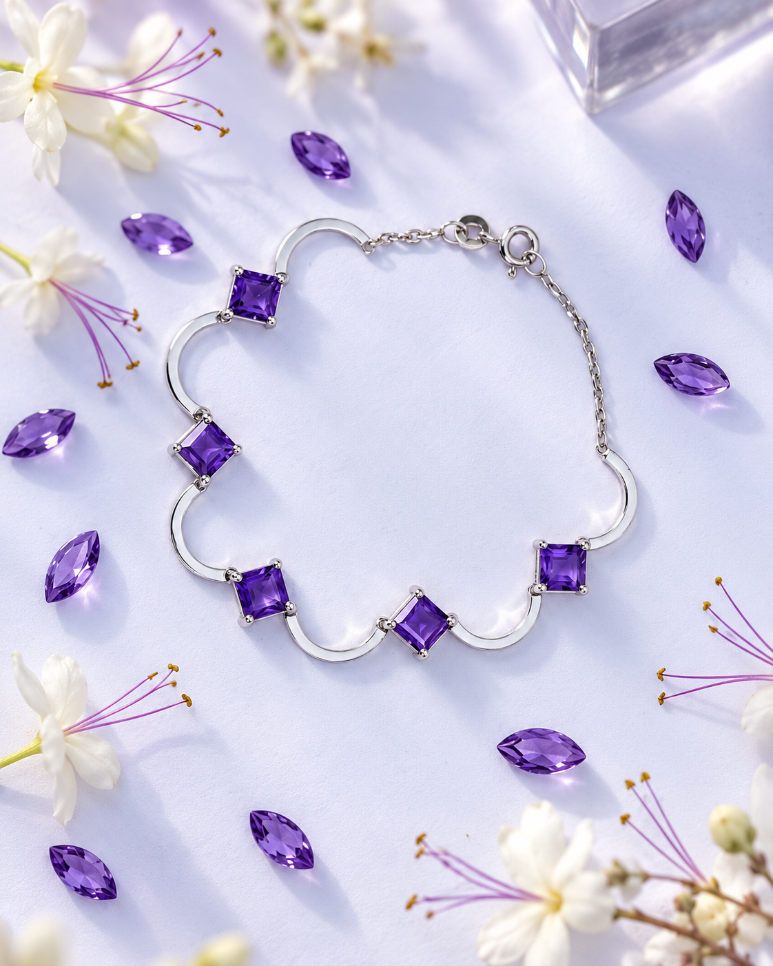 A silver-toned bracelet with five square-cut amethyst gemstones, arranged in a flat-lay on a white surface with scattered purple crystals and white flowers.