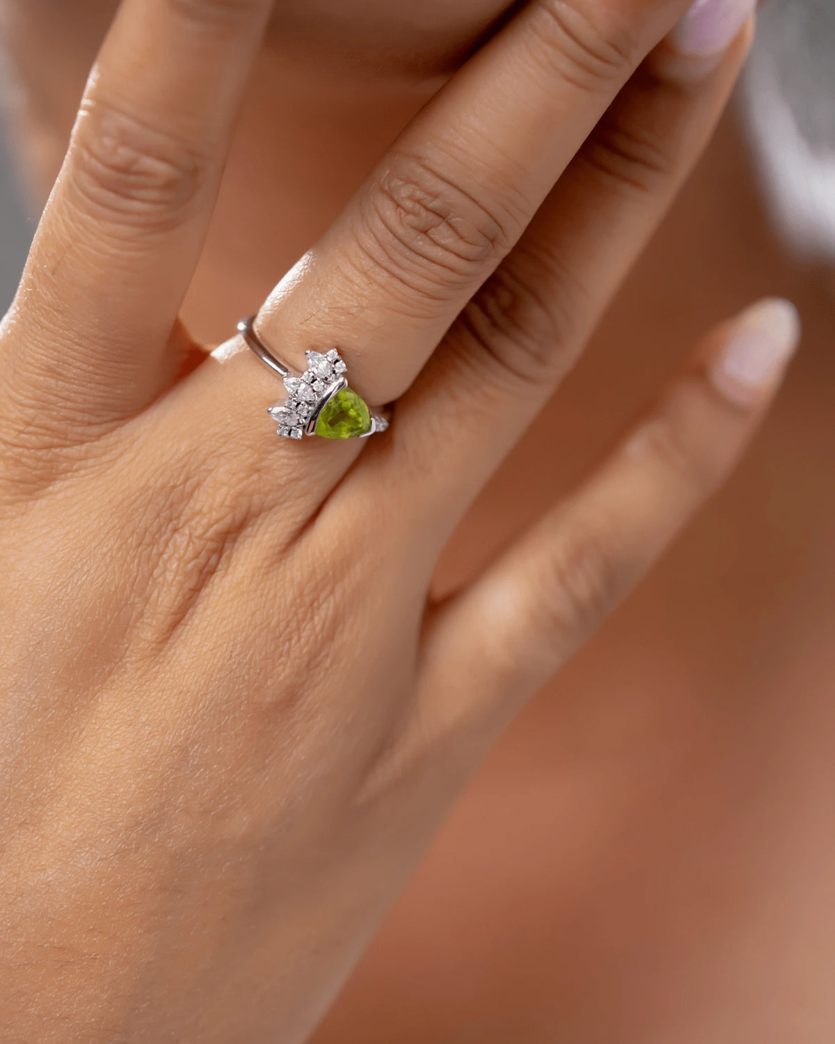 Hand wearing a ring with a green peridot gemstone on a blurred background
